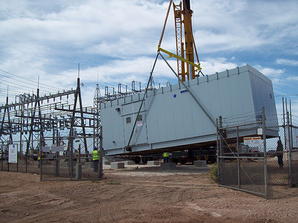 A control house is being lowered onto its foundation at a substation construction site.