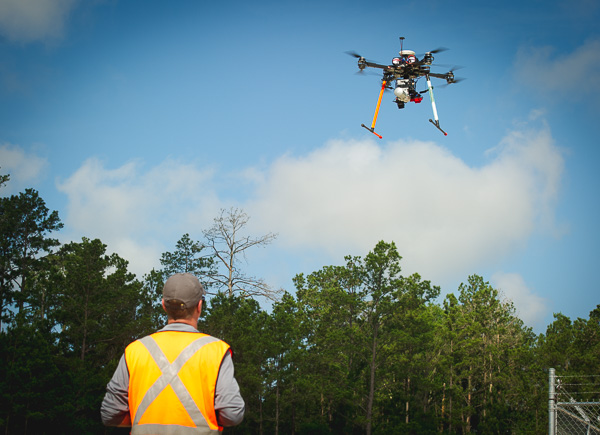 Unmanned aerial vehicle pilot operates a drone. Trees in background.